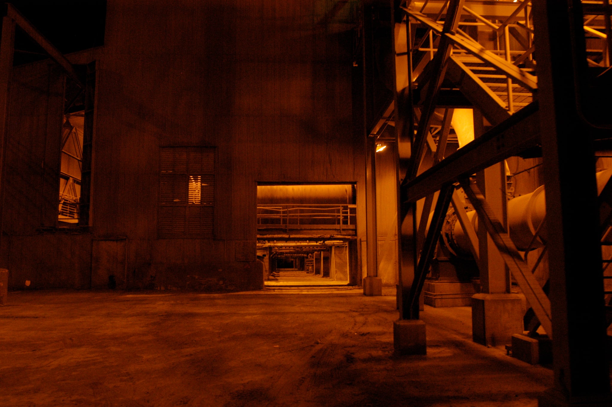An industrial plant at night, its structure and stack lit warm orange against the dark.